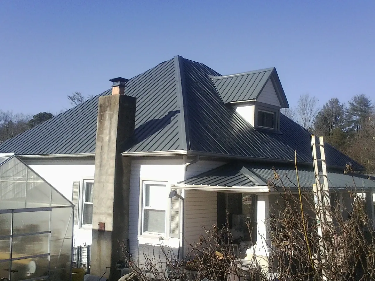 Dark blue standing seam metal roof on a white farmhouse with dormer — Slate & Tile Roof Repair by Roofing Brothers in Como