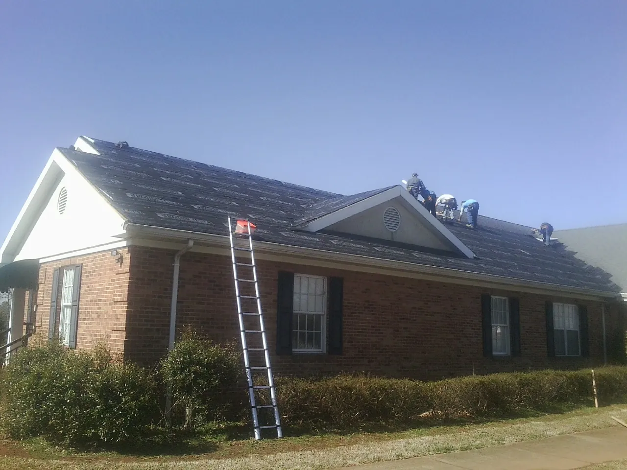 Crew tearing shingles off a brick ranch roof with a ladder set — Metal Roof Repair work by our crew in Como