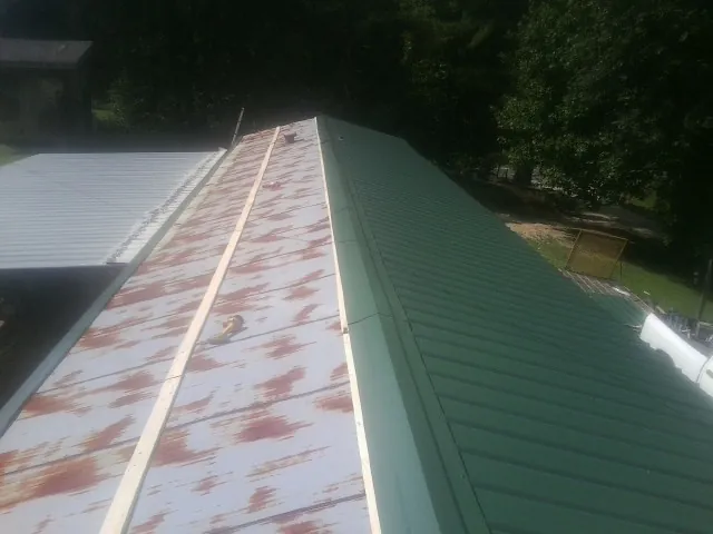 Old rusted panels beside newly installed green metal roofing — Wind Damage Roof Repair by Roofing Brothers in Como