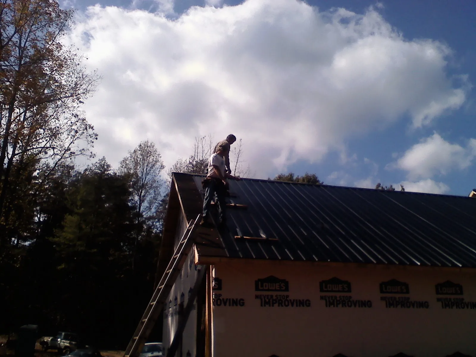 Roofer fastening dark metal panels high against a cloudy sky, from a Roof Inspection job in Como
