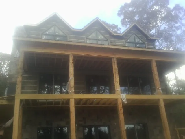 Dormers and porch framing on a large log home under construction — Roof Coating work by our crew in Como