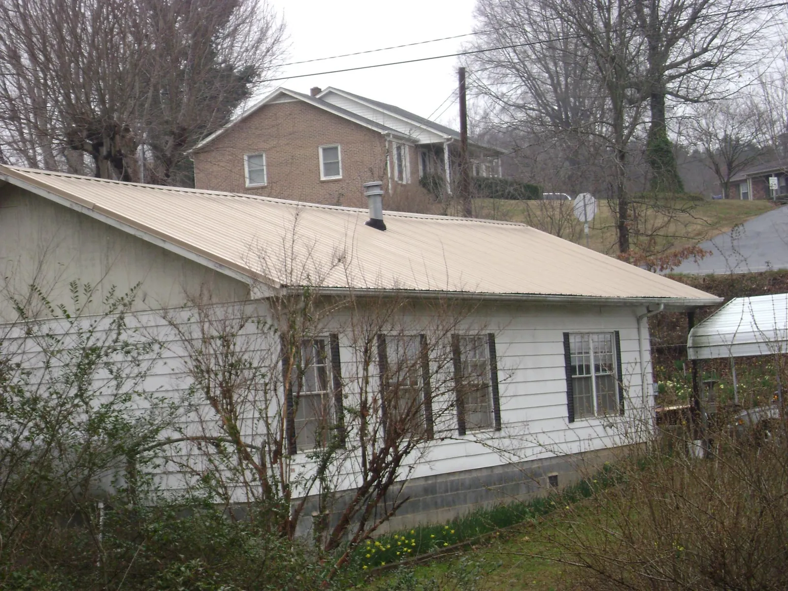 Tan metal roof on a white sided house set into a hillside — Commercial Roofing by Roofing Brothers in Como