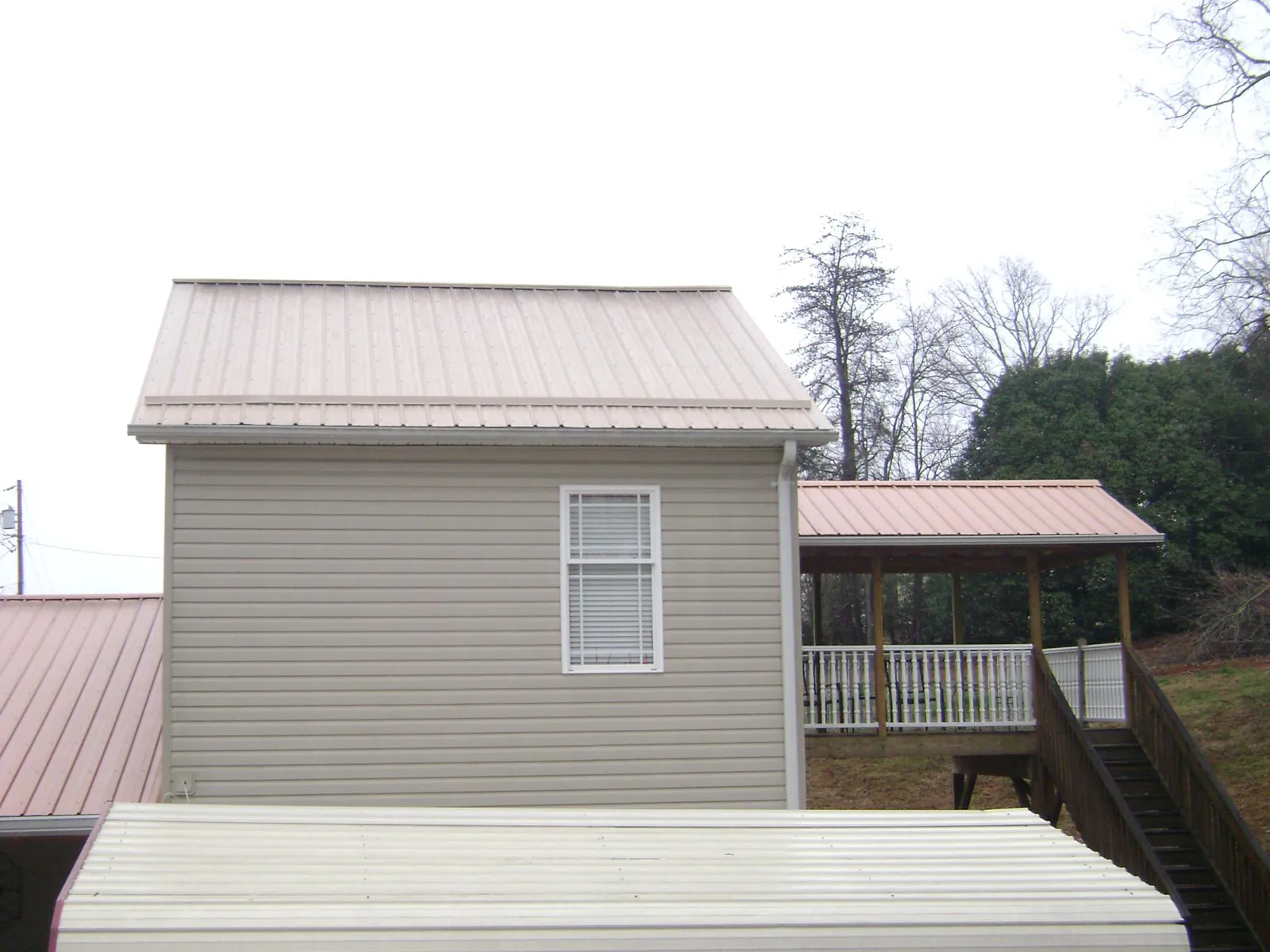 Tan metal roofs on a two story addition and attached porch, from a Roof Replacement job in Como